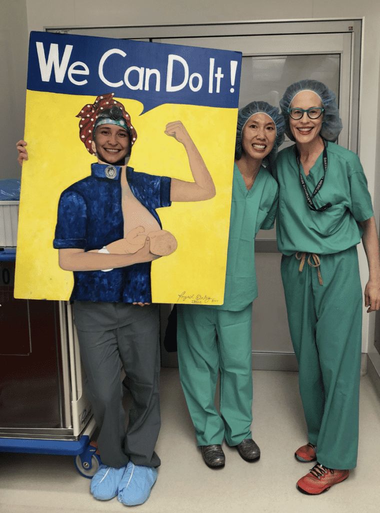 Dr. Katrina Mitchell with colleagues, one holds sign with face cutout - Rosie the riveter saying We Can Do It
