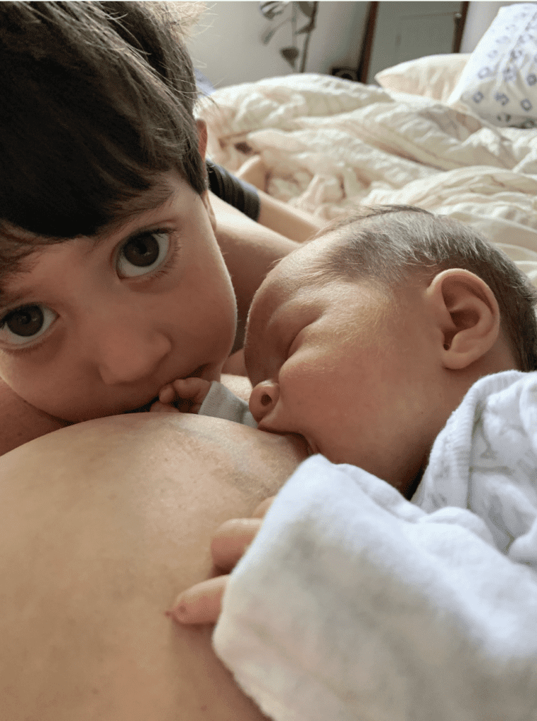 Baby nursing with older sibling nearby