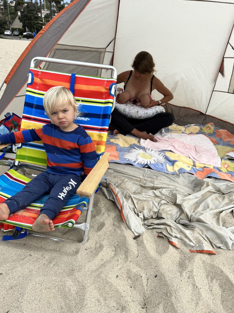 Mom breastfeeding twins at beach with older brother